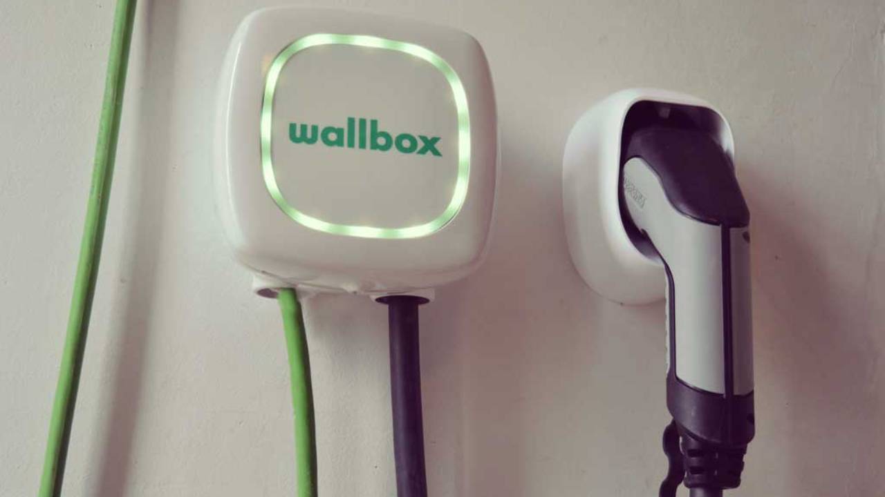 Una persona installa un caricatore per auto elettrica in un garage, con attrezzatura elettrica e strumenti